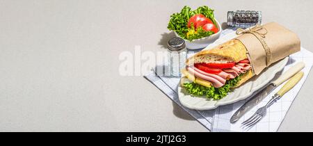 Panini sandwich con prosciutto, insalata croccante e verdure. Cibo sano per andare concetto, pranzo o opzione snack. Trendy luce dura, ombra scura, conca di pietra Foto Stock