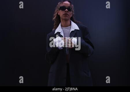 elegante donna afroamericana in occhiali da sole regolazione tuta oversize vicino a parete blu scuro Foto Stock