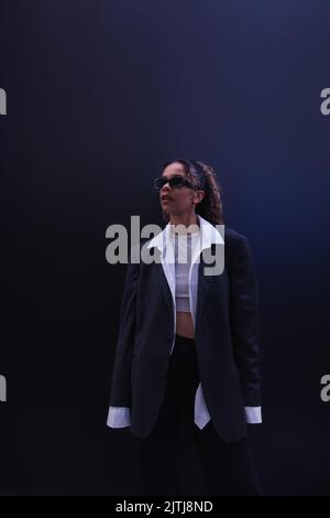 elegante donna afroamericana in occhiali da sole e tuta oversize su blu scuro Foto Stock