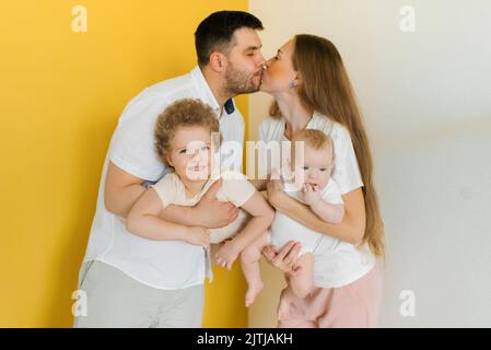 I giovani genitori baciano mentre tengono i loro figli tra le braccia Foto Stock