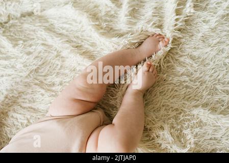 Pancia e gambe di un neonato in un bodysuit sdraiato su un letto leggero, vista dall'alto Foto Stock