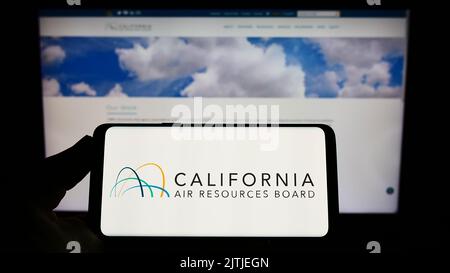 Persona che tiene in mano lo smartphone con il logo del California Air Resources Board (CARB) sullo schermo davanti al sito Web. Messa a fuoco sul display del telefono. Foto Stock