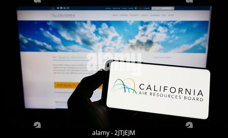 Persona che tiene un telefono cellulare con il logo del California Air Resources Board (CARB) sullo schermo davanti alla pagina Web. Messa a fuoco sul display del telefono. Foto Stock