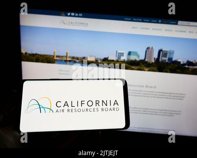Persona che tiene il cellulare con il logo del California Air Resources Board (CARB) sullo schermo di fronte alla pagina web. Messa a fuoco sul display del telefono. Foto Stock
