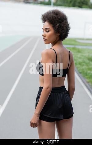 Giovane sportivo afro-americano in abbigliamento sportivo nero in piedi sullo stadio Foto Stock