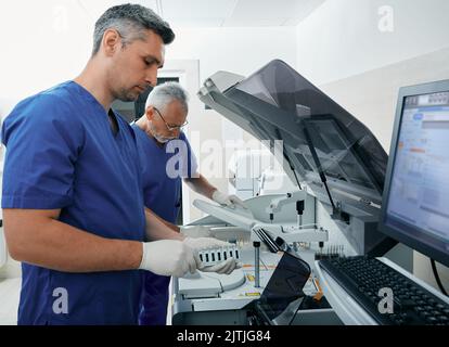 Assistenti di laboratorio che caricano i campioni di sangue nell'analizzatore automatico biochimico del sangue. Moderno laboratorio di ricerca medica e tecnici di laboratorio Foto Stock