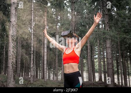 Donna sportiva che indossa una cuffia per realtà virale che si esercita in una foresta virtuale. Foto Stock