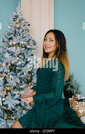 Giovane bella donna in macchina fotografica, trucco e capelli styling con un cerchio sullo sfondo di un albero di Natale bokeh Foto Stock