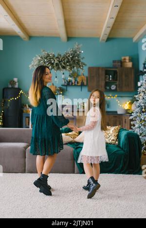 Mamma e figlia che tengono le mani nel soggiorno della casa, decorata per Natale Foto Stock