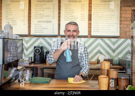 Barista allegro che si pone per la fotocamera durante la pulizia del piano di lavoro Foto Stock