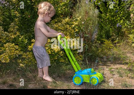 Un ragazzino spinge un tosaerba soffiando delle bolle nel giardino Foto Stock
