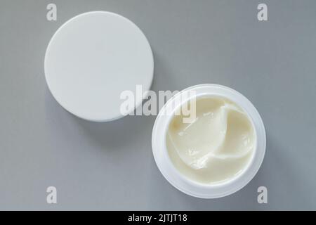 Contenitore aperto di crema per trattamenti di bellezza con tappo su sfondo grigio. Vista dall'alto Foto Stock