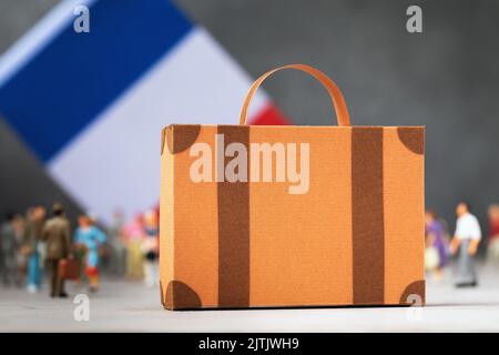 Valigia di cartone, personaggi di giocattoli di plastica e una bandiera su uno sfondo astratto, un concetto sul tema del trasferimento o della migrazione verso la Francia Foto Stock