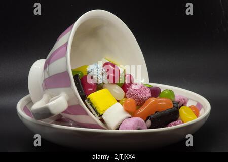 Teacup rosa e bianco e piattino con dolci vari. Quanto zucchero è contenuto nella vostra bevanda? Foto Stock