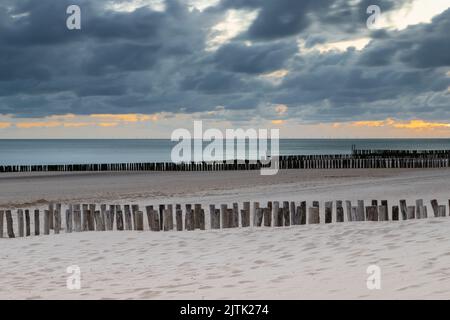 Un tramonto spettacolare su una spiaggia di sabbia e il mare del Nord nei Paesi Bassi visto dalla spiaggia di Zoutelande, Zeeland con i tipici demolitori di legno Foto Stock