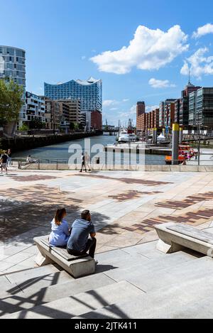 La gente si trova e si siede sulle terrazze di Magellano al sole estivo e guarda fuori sull'Elbphilharmonie e sull'Hafenity di Amburgo, Amburgo, Germania Foto Stock