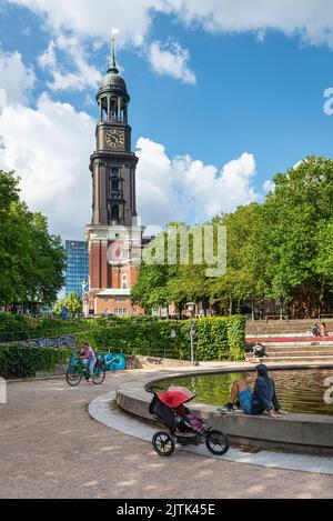 Un uomo con un pram siede di fronte ad una fontana sul Michelwiese di fronte alla chiesa di San Michele ad Amburgo, in Germania, in un giorno estivo Foto Stock