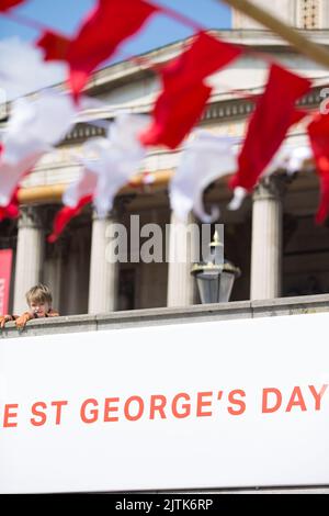 Uno spettatore è visto dietro le decorazioni mentre le persone si riuniscono per le celebrazioni del giorno di San Giorgio a Trafalgar Square, nel centro di Londra. Foto Stock