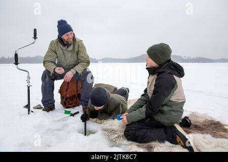 Uomo sorridente che parla con il ragazzo mentre il figlio fa la pesca del ghiaccio al lago ghiacciato Foto Stock