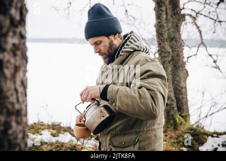 Uomo maturo in abiti caldi che versa il tè dal bollitore Foto Stock