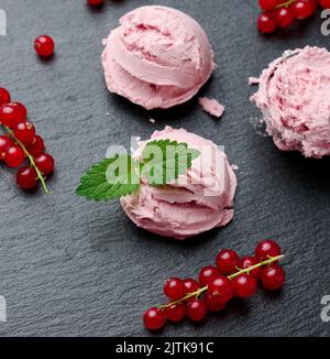 Palline di gelato rosa su un asse di pietra nera, bacche di ribes rosso nelle vicinanze, vista dall'alto Foto Stock