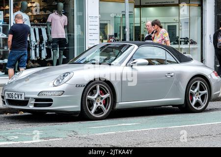 Kingston-upon-Thames, Londra, Regno Unito, agosto 29 2022, Convertable Silver Porsche 911 parcheggiata su Una strada principale con gli acquirenti che navigano in Shop Windows Foto Stock