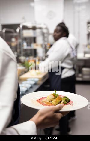 Vista posteriore dello chef che porta cibo nel piatto della cucina del ristorante Foto Stock