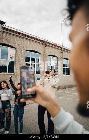 Giovane uomo che fotografa gli amici attraverso il telefono cellulare in strada in città Foto Stock