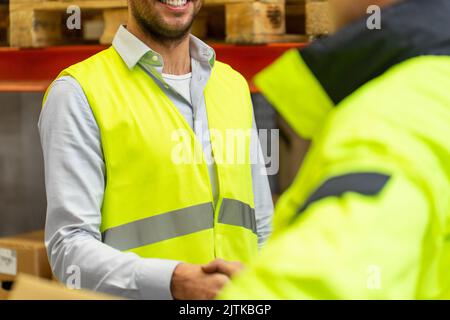 Gli uomini in giubbotti di sicurezza si stringono la mano a magazzino Foto Stock