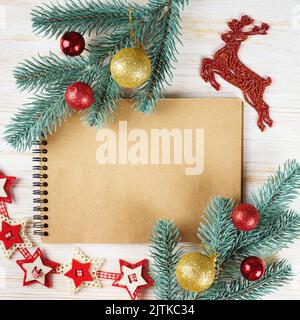 Notebook vuoto con decorazioni natalizie. Rami d'albero di Natale con palle rosse e d'oro, cervi, ghirlanda rossa e spazio copia su sfondo di legno bianco Foto Stock