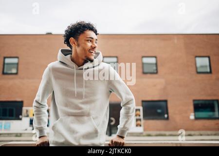 Felice giovane uomo che guarda lontano mentre si trova di fronte all'edificio Foto Stock