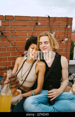 Sorridenti amici maschi e femmine seduti con gli occhi chiusi durante la festa sul tetto Foto Stock