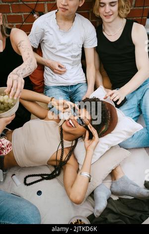 Donna felice che indossa occhiali da sole sdraiati dagli amici durante la festa sul tetto Foto Stock