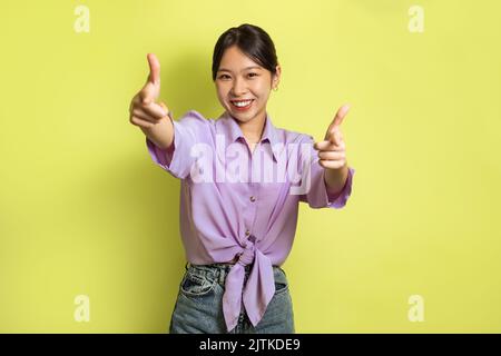 Felice Asian Lady che punta le dita alla fotocamera su sfondo giallo Foto Stock