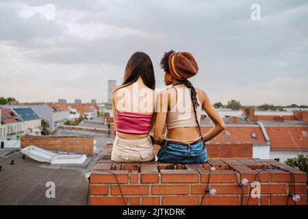 Vista posteriore delle giovani donne sedute sul tetto Foto Stock