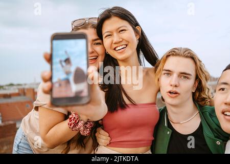 Ritratto di una giovane donna che mostra lo smartphone mentre è in piedi tra gli amici Foto Stock