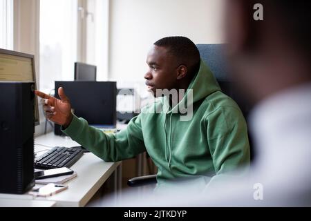 Tirocinante maschile in camicia con cappuccio che indica lo schermo del desktop mentre discute in ufficio Foto Stock