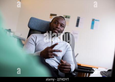 Uomo d'affari che gestura mentre si siede sulla sedia in ufficio Foto Stock
