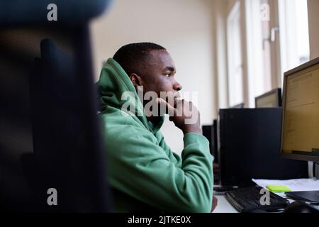 Studente maschio preoccupato con mano sul mento guardando il computer in ufficio Foto Stock