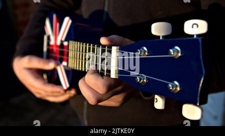 Primo piano delle mani che giocano un ukelele rosso, bianco e blu Foto Stock