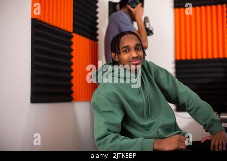 Ragazzo con felpa con cappuccio verde seduto in studio di registrazione Foto Stock