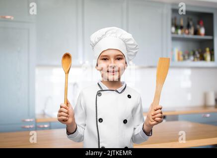 ragazzo sorridente in toque dello chef con cucchiaio e spatola Foto Stock