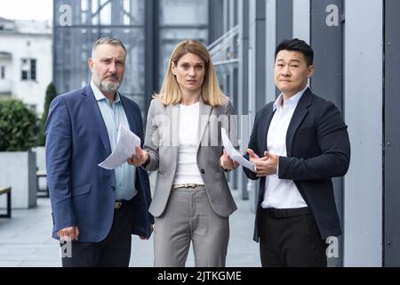 Boss di affari femminile frustrato con i documenti che guardano la macchina fotografica, il team dei colleghi diversi fuori dall'ufficio edificio turbato con il risultato del rapporto di lavoro Foto Stock