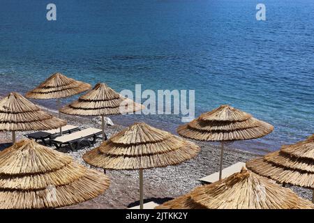 Spiaggia di ciottoli vuota con ombrelloni in vimini e sedie a sdraio. Pittoresca vista sul mare con acqua blu, resort estivo Foto Stock