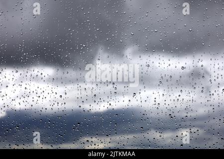 Gocce di pioggia sul vetro della finestra su sfondo sfocato del cielo con nuvole di tempesta. Bellissime gocce d'acqua, tempo piovoso Foto Stock