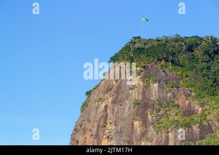 Timone in pietra con bandiera del Brasile in cima, visto dalla spiaggia di timone a Rio de Janeiro Brasile. Foto Stock