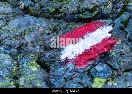 Sentiero escursionistico alpino in Austria, segnato con bandiera austriaca dipinta su una roccia solida lungo il percorso Foto Stock