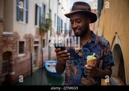 Un turista a Venezia usa il suo smartphone mentre mangia un gelato, concetto di tecnologia in vacanza Foto Stock