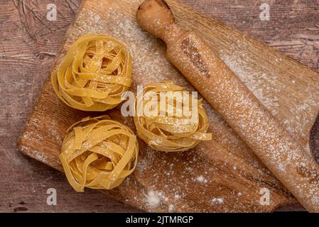 Fotografia alimentare di pasta cruda, tagliatelle, fettuccine, macro, rolling pin, scheda Foto Stock