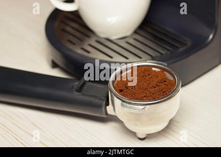 Portafiltro per macchina da caffè con macinato e tazza di caffè su fondo in legno bianco. Foto Stock